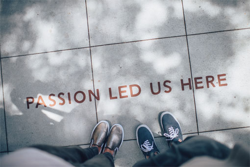 Two pairs of shoes standing on a paved sidewalk that reads, "Passion led us here"