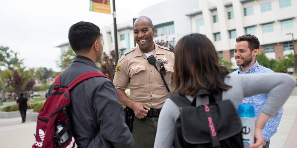 Los Angeles County Sherriff and School Campus Liaison smiling and talking to two teen students