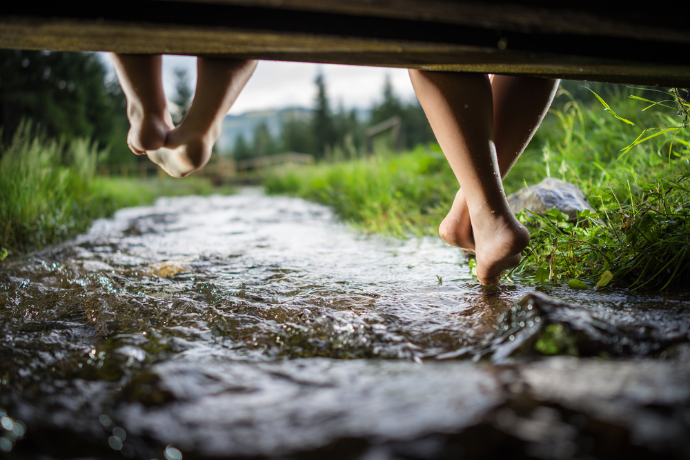 children-sitting-on-a-wooden-bench-with-feet-dangling-over-a-mountain-creek