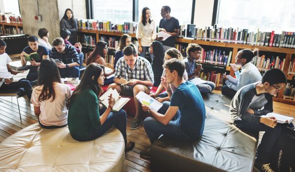 Group of diverse teen students talking to each other in a library